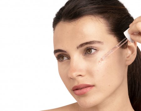 Iliustracija, kurioje moteris tepasi serumą ant veido, pabrėžiant hialurono rūgšties naudą odos priežiūrai.