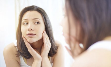 Moteris tikrinasi savo odą veidrodyje